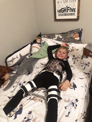 Jadon smiling lying in bed wearing his Scottish Rite brace