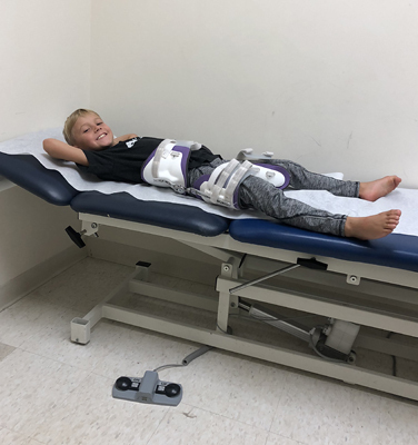 Jadon smiling lying down on an exam table wearing a brace