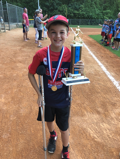Preston on crutches on a baseball field with a medal and trophy