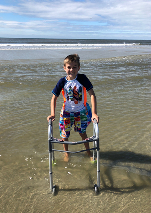 Preston in shallow water at the beach while using his walker