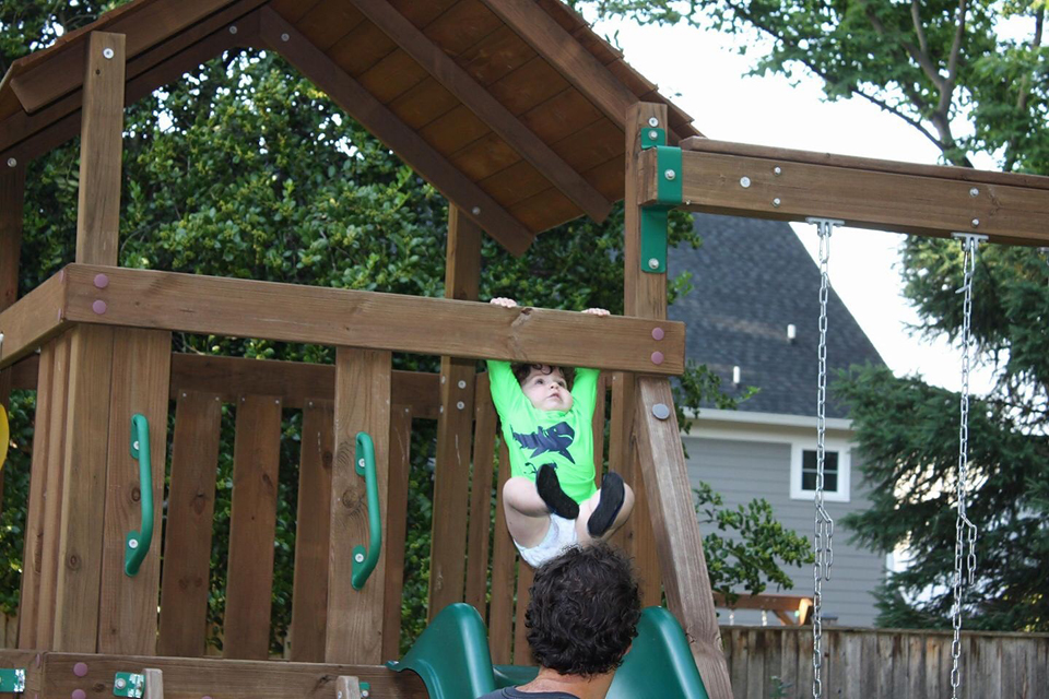 Ross hanging from a wood beam above a sliding board on a swing set