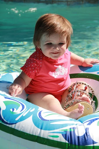 Emma as a toddler wearing an external fixator on one leg in a float in a pool