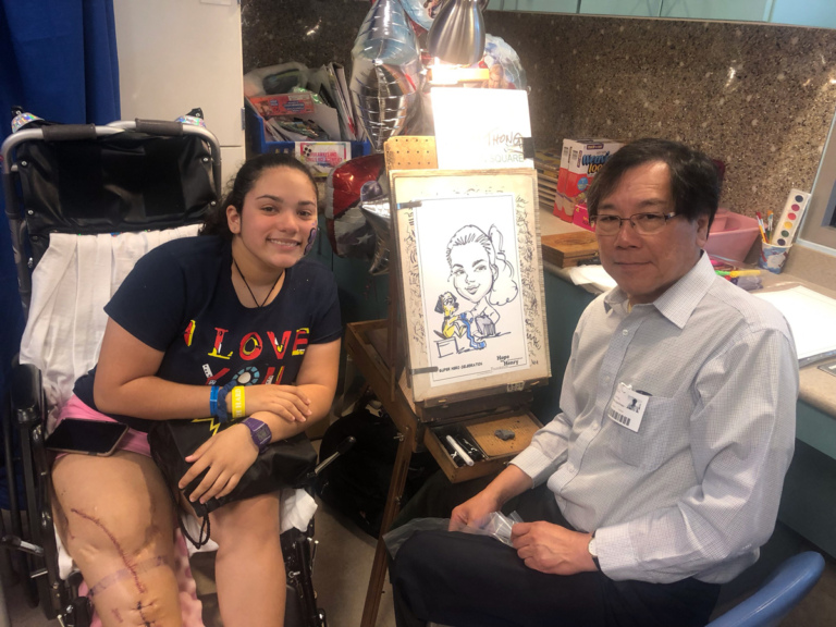 Girl patient in wheelchair and caricature artist smiling showing off her completed caricature of her with a dog