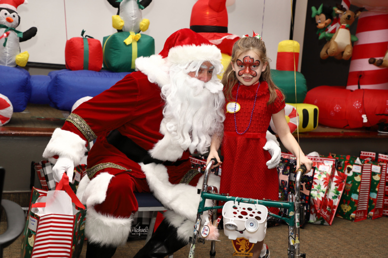 Young girl with gingerbread man face paint using a walker next to Santa Claus