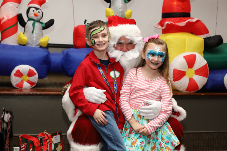 Girl and boy with face paint smiling on Santa’s lap