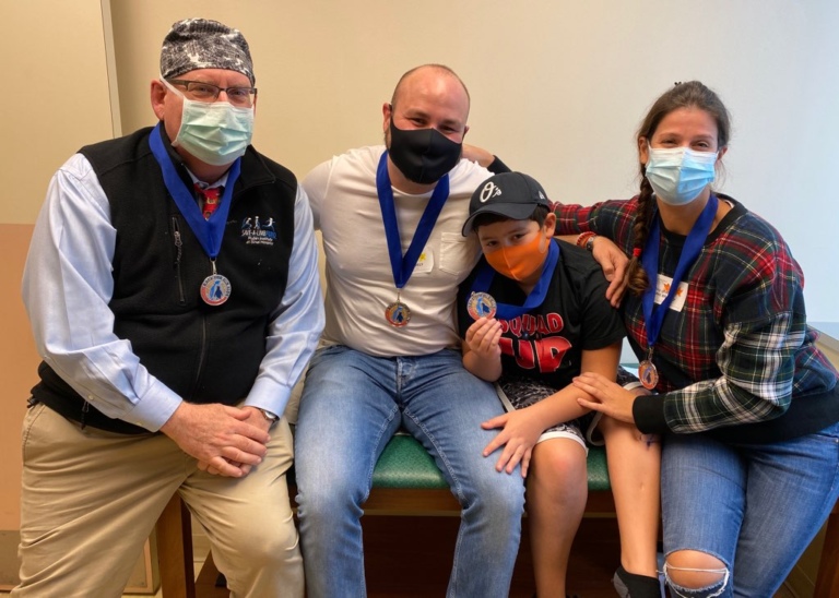 Nicolai and his family smiling with Dr. Herzenberg while wearing masks and Race for Our Kids medals