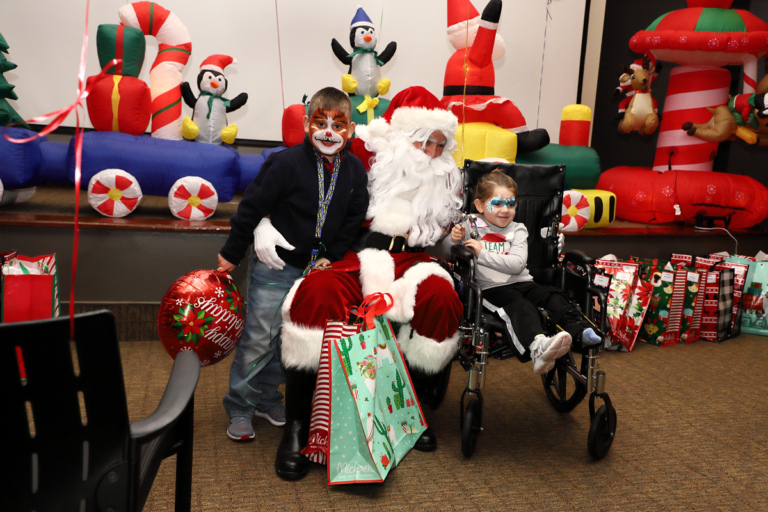 Face-painted boy and girl in a wheelchair smiling with Santa Claus