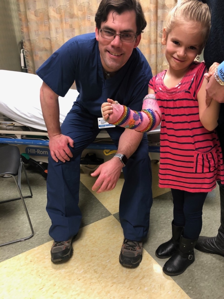 Emma with a bedazzled cast on her arm smiling with Dr. McClure
