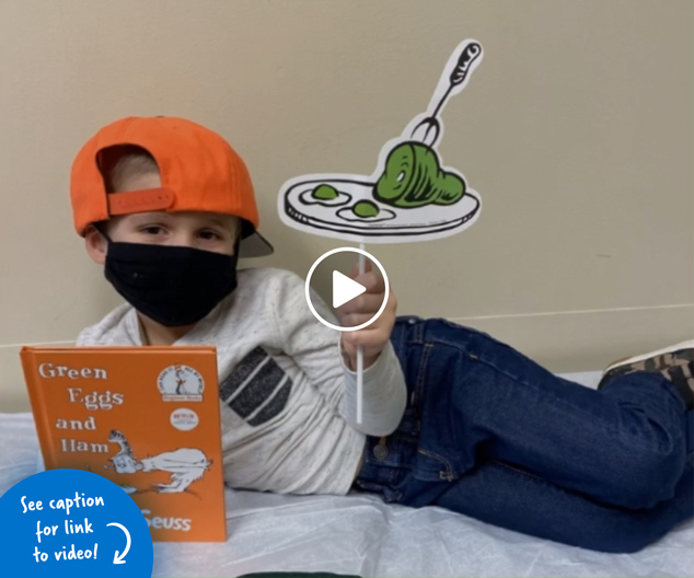 A boy laying on an exam table holding the book Green Eggs and Ham by Dr. Seuss.