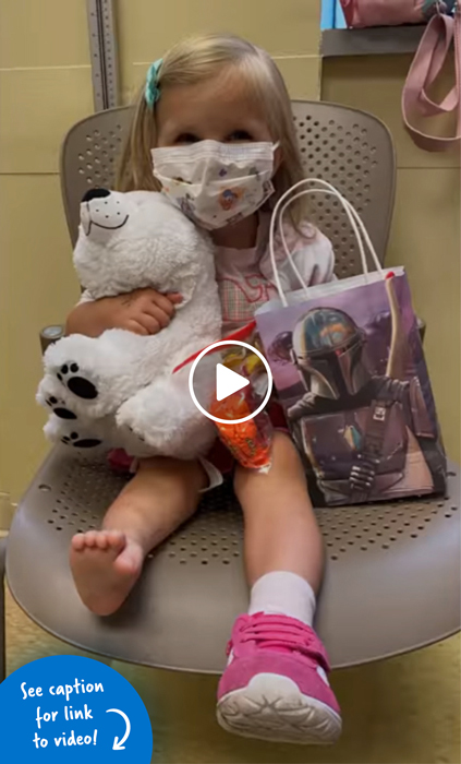 A girl sitting in a chair holding a stuffed polar bear and a Mandalorian-themed bag