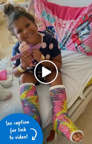 A little girl with colorful casts on both of her legs holding a stuffed unicorn and sitting in a hospital bed