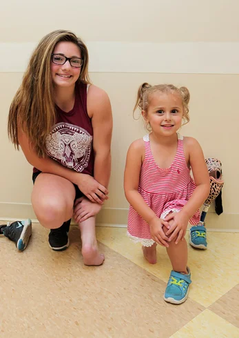 Brooklynn and Danica, two patients who have undergone the rotationplasty procedure, kneeling to show how their feet are used as knee joints.