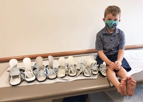 Evan sitting with a series of his clubfoot boots that he is donating for other children