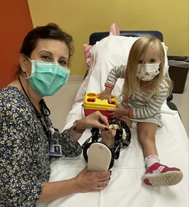 A girl with an external fixator on her leg sitting on a bed with a physical therapist performing physical therapy on her