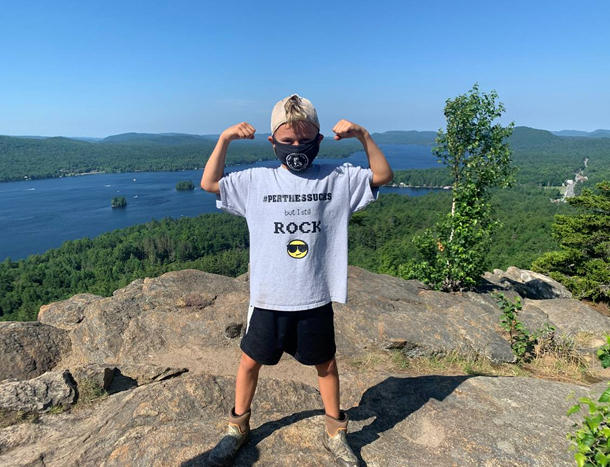 Jadon posing in a champion stance wearing a Perthes Sucks shirt while hiking