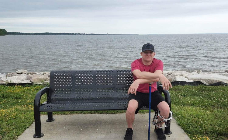Andrew wearing an external fixator sitting on a bench by the Chesapeake Bay