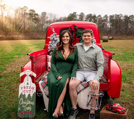 Andrew wearing an external fixator sitting in the back of a red truck with his wife for a Christmas picture