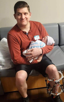 Andrew wearing an external fixator sitting holding his son in the delivery room