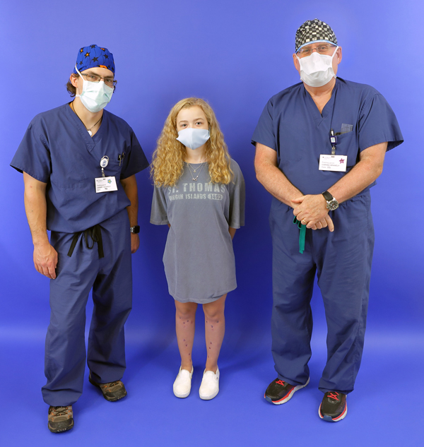 Bridget with straightened legs after treatment standing between Dr. McClure and Dr. Herzenberg