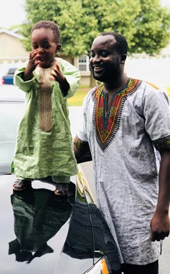 Ebou smiling with his young son on a car