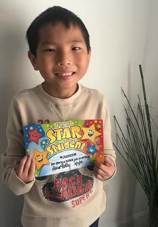 James smiling showing his writing award certificate from school after surgeries