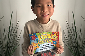 James smiling showing his writing award certificate from school after surgeries