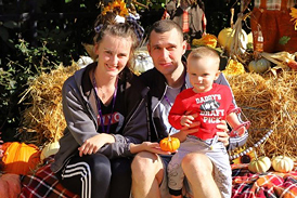 Kacper with his mother and father posing for a picture next to an autumn display
