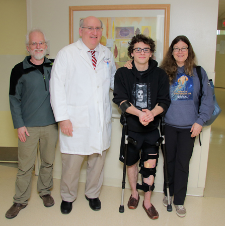 Keagan standing with a brace on his leg smiling with his parents and Dr. John Herzenberg