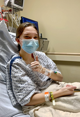 Lexie giving the thumbs up signal in her hospital bed before surgery