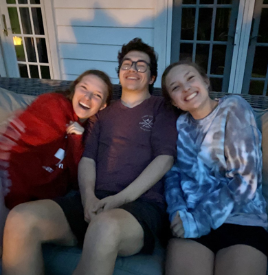 Lexie and her twin sister and brother all smiling while sitting on a couch
