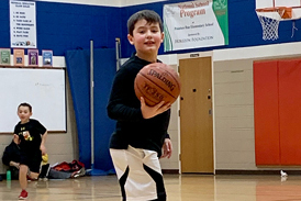 Nicolai playing basketball on a court in a gym with other children