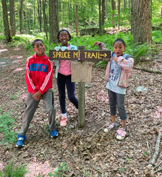 Sudan and two girls outside by a hiking trail sign marked steep
