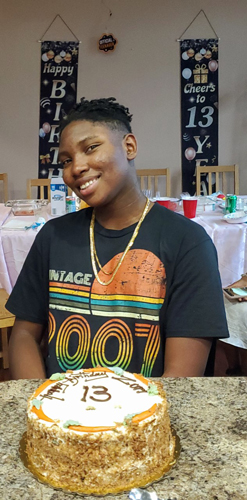 Zuri smiling in front of his cake for his 13th birthday