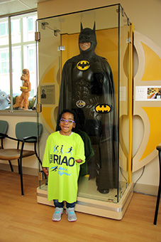 Kennedee as a young girl in a long RIAO t-shirt in front of the ICLL clinic waiting room Batman display