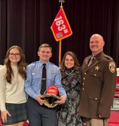 Matthew as an adult standing with his family at the ceremony where he became an official firefighter