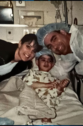 Ken as a very young boy on a hospital bed with his parents on either side before going into surgery